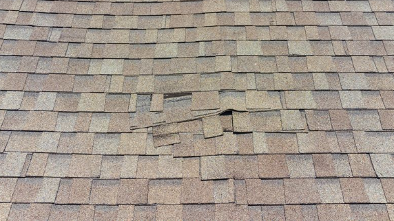 Damaged roof with missing and broken asphalt shingles. Brown and tan colors are visible.