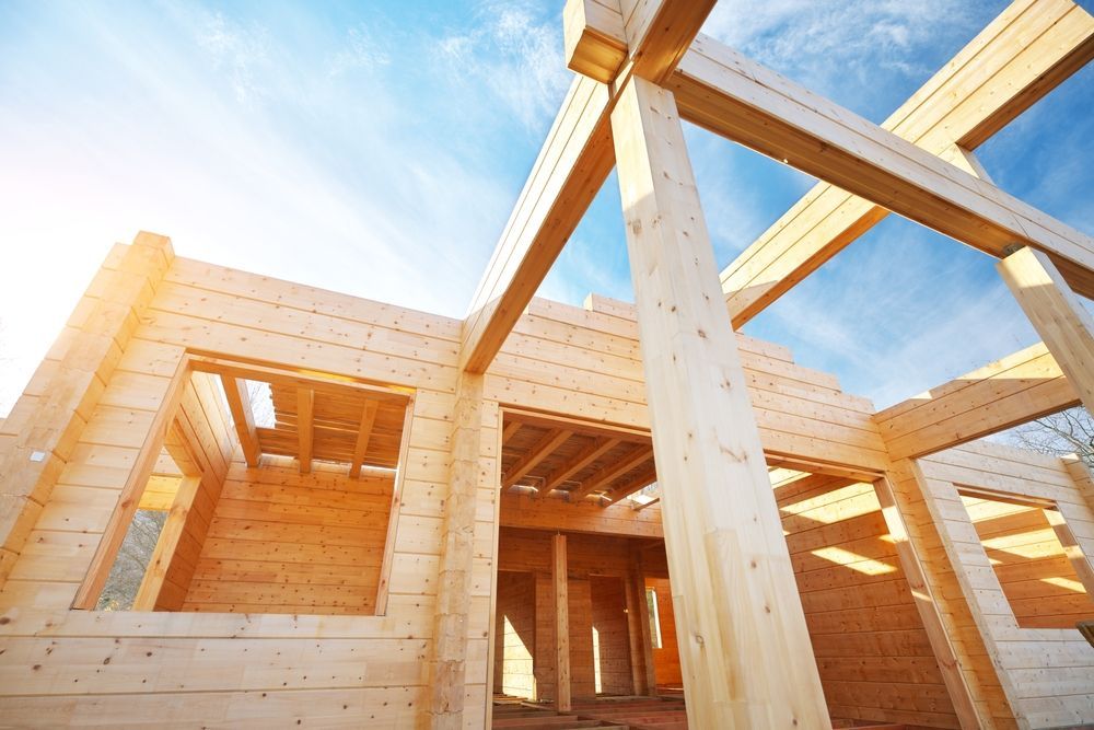 Wooden house frame under construction, bright sunlight, blue sky.