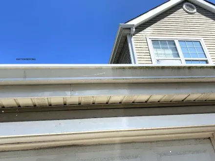 White gutter mounted along the edge of a tan vinyl-sided house with a clear blue sky in the background.