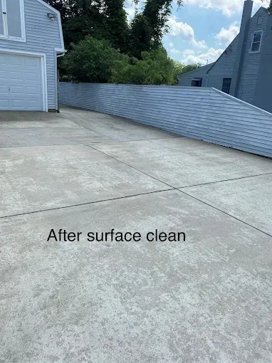 A light-colored concrete driveway next to a gray house after being pressure washed.