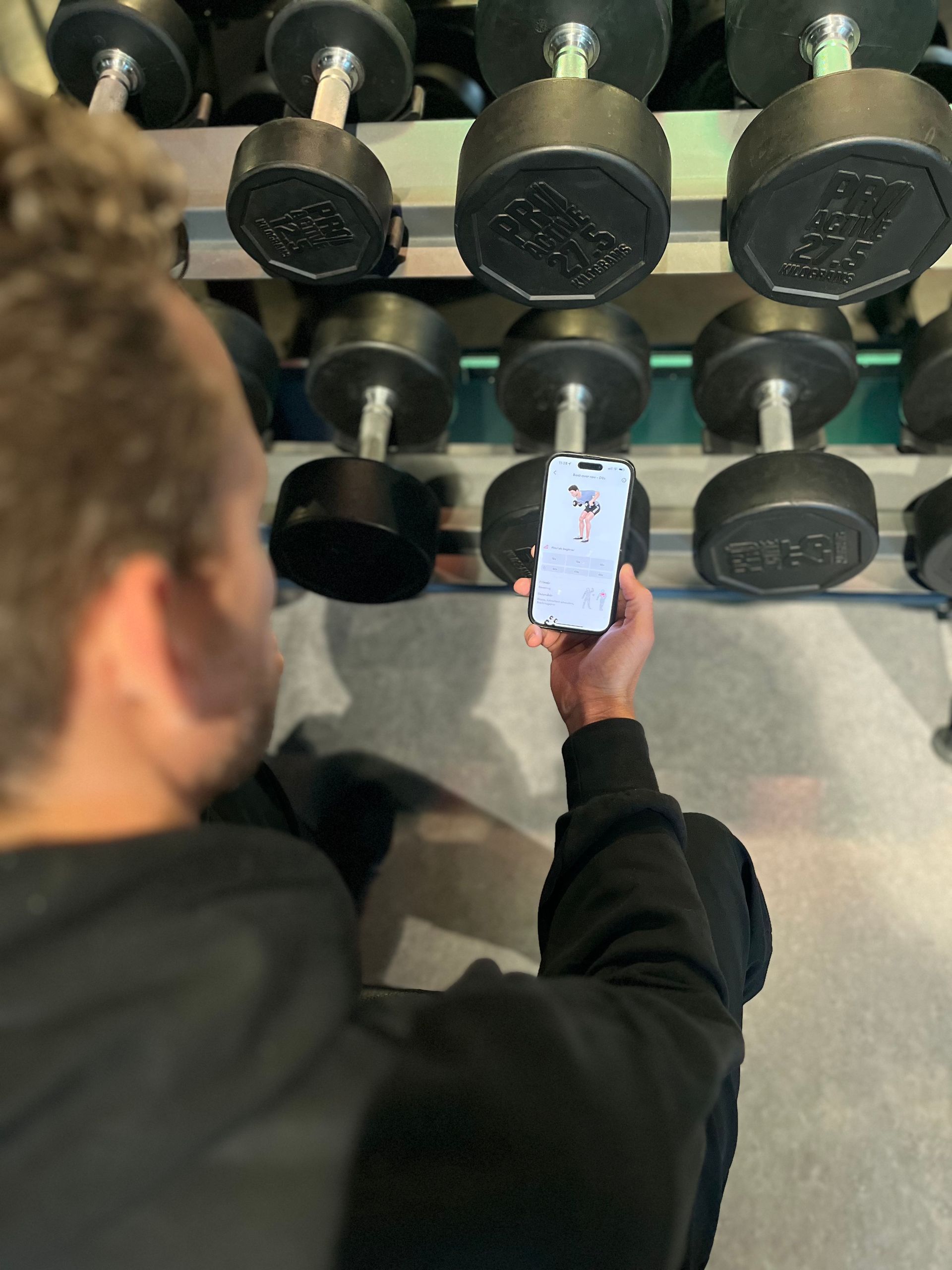 Een man houdt een mobiele telefoon vast voor een rek met halters