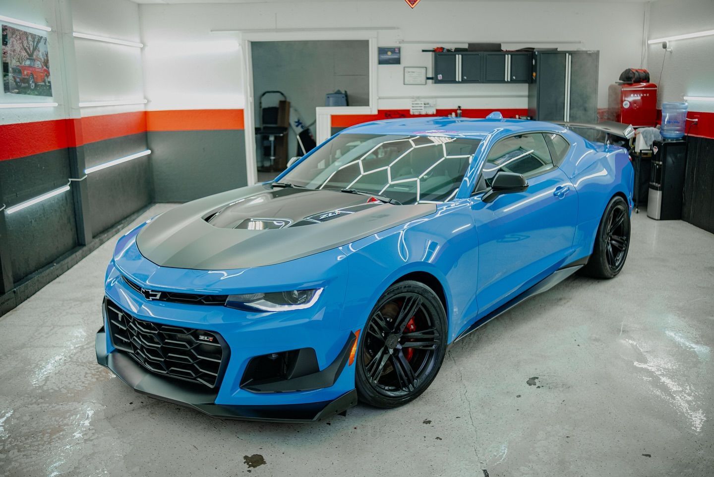 Bright blue Chevrolet Camaro sports car in a garage, with a black hood, black rims, and red accents.