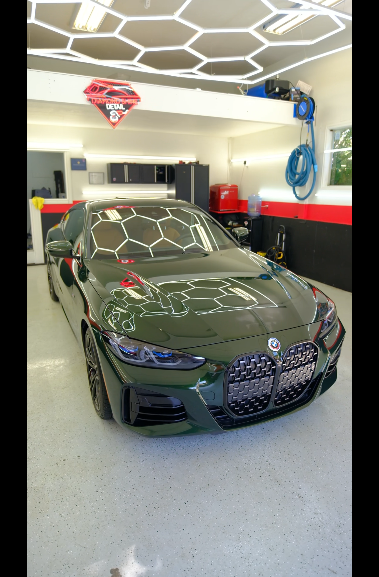 Green BMW car in a brightly lit garage, with hexagonal lighting overhead.