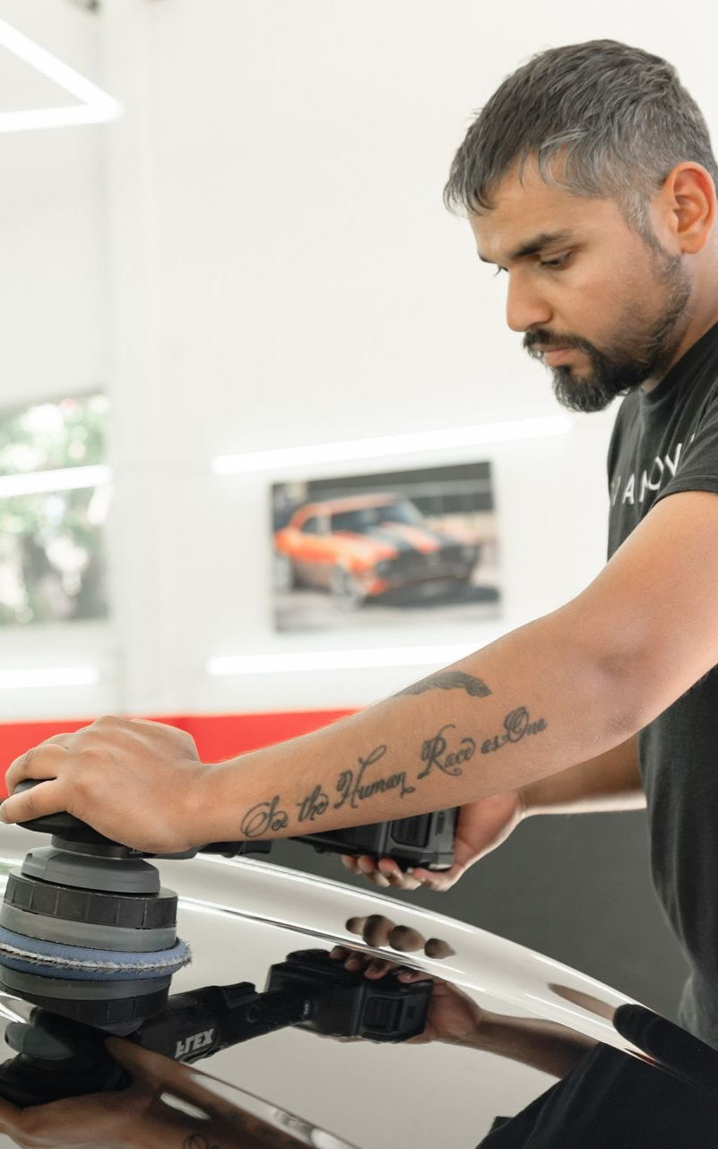 Man using a polishing tool on a car's hood in a garage.