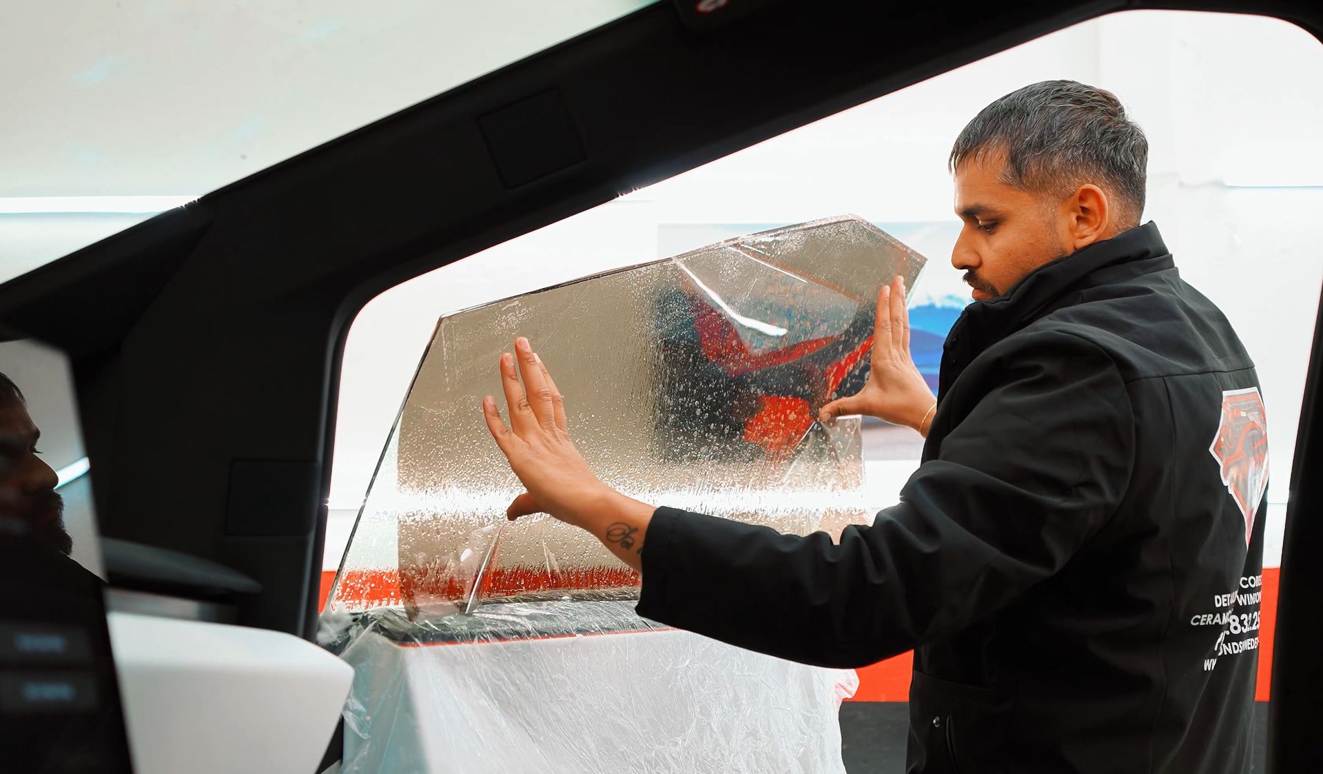 A person applying window tint to a car window, indoors. The person is holding the tint in place.