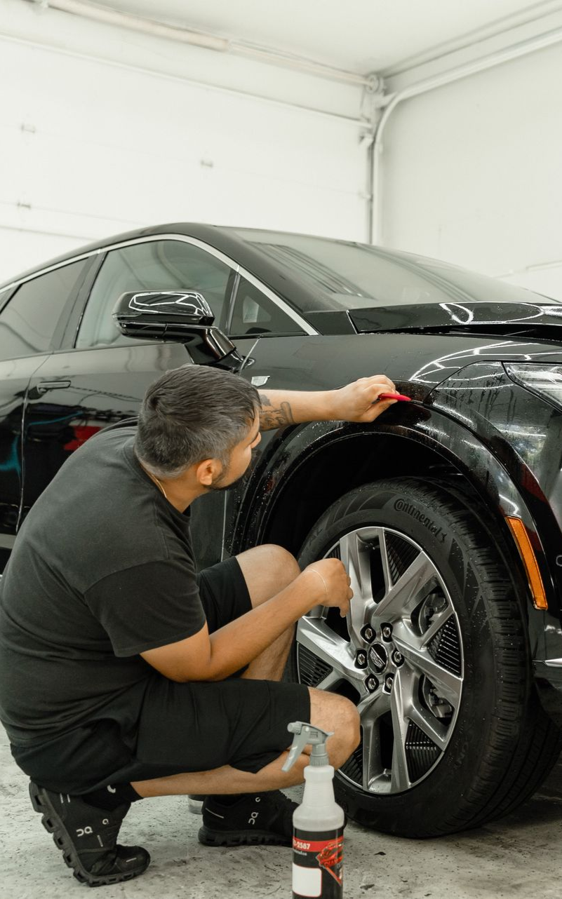 Person applying protective film on the fender of a black car in a garage.