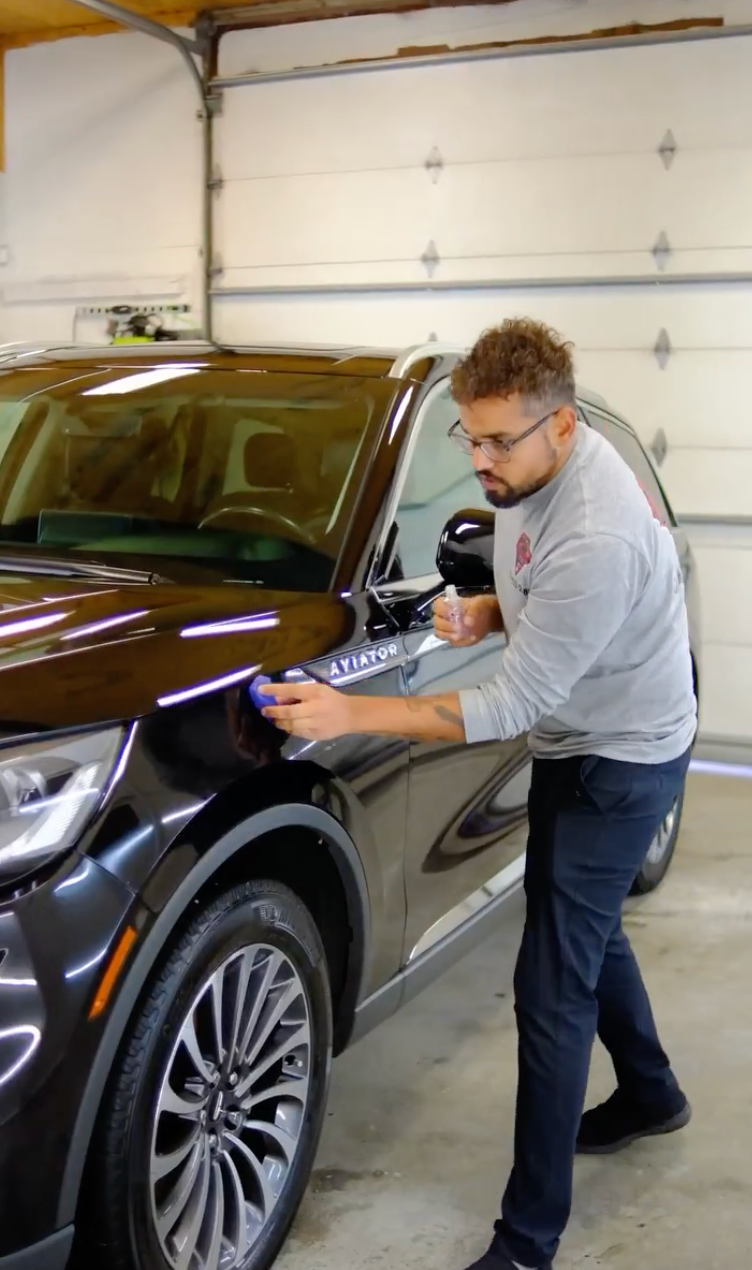 A man is polishing a black car in a garage.