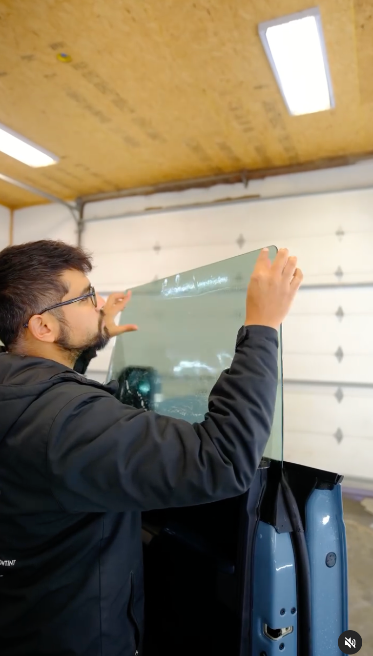 Man installing tinted car window in a garage.