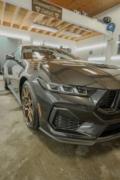A black car is parked in a garage under a sign that says diamond shine detail.