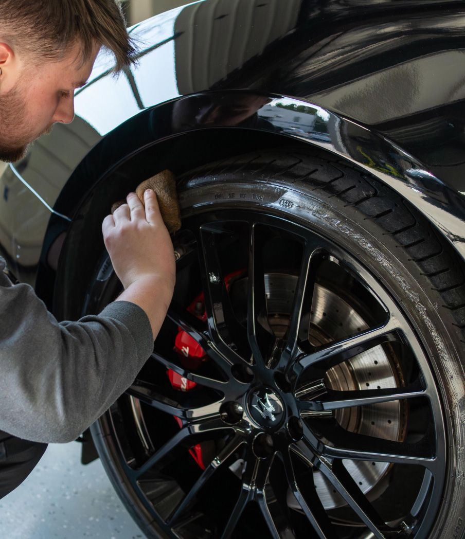 Person cleaning a black car's tire with a sponge, showing a shiny wheel and red brake calipers.