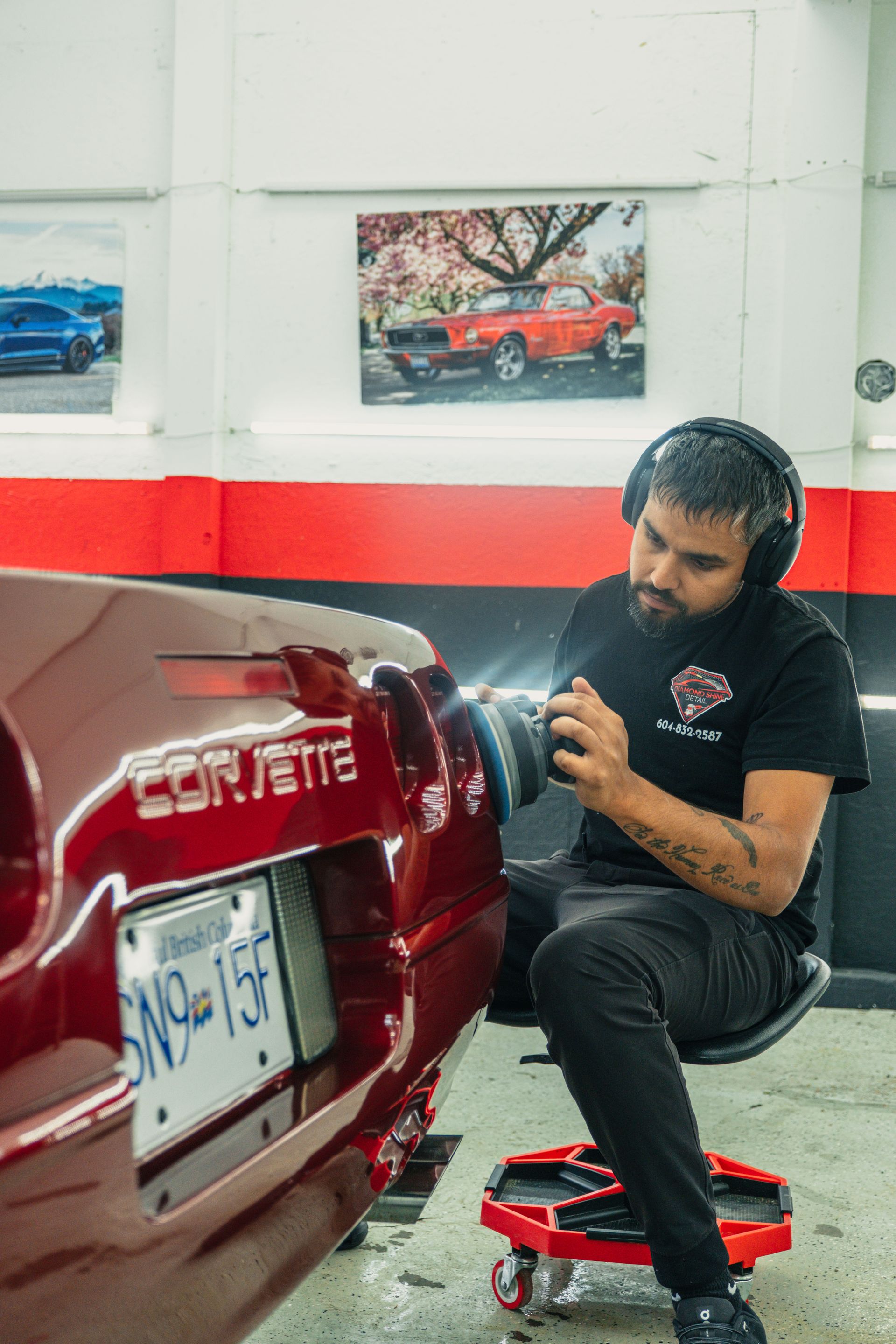 Man polishing a red Corvette in a garage, wearing headphones. The license plate is visible.