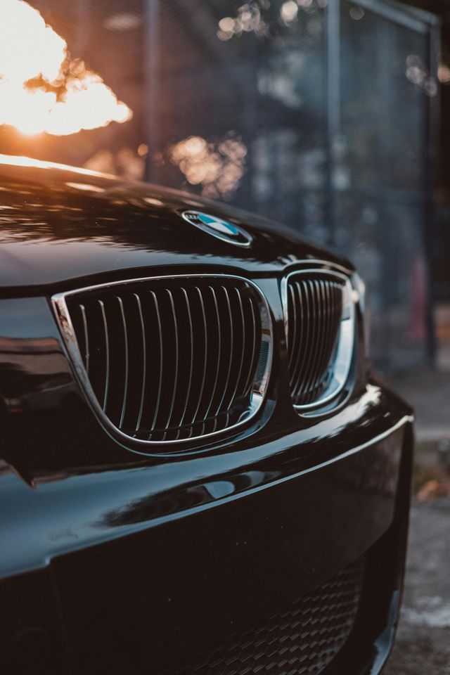 Black BMW car front, shiny, with silver grille, in outdoor setting. Sunlight.