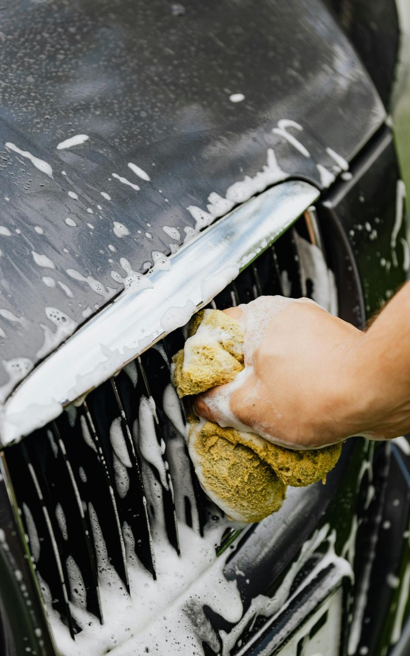 Hand washing a black car's front grill with a soapy sponge.
