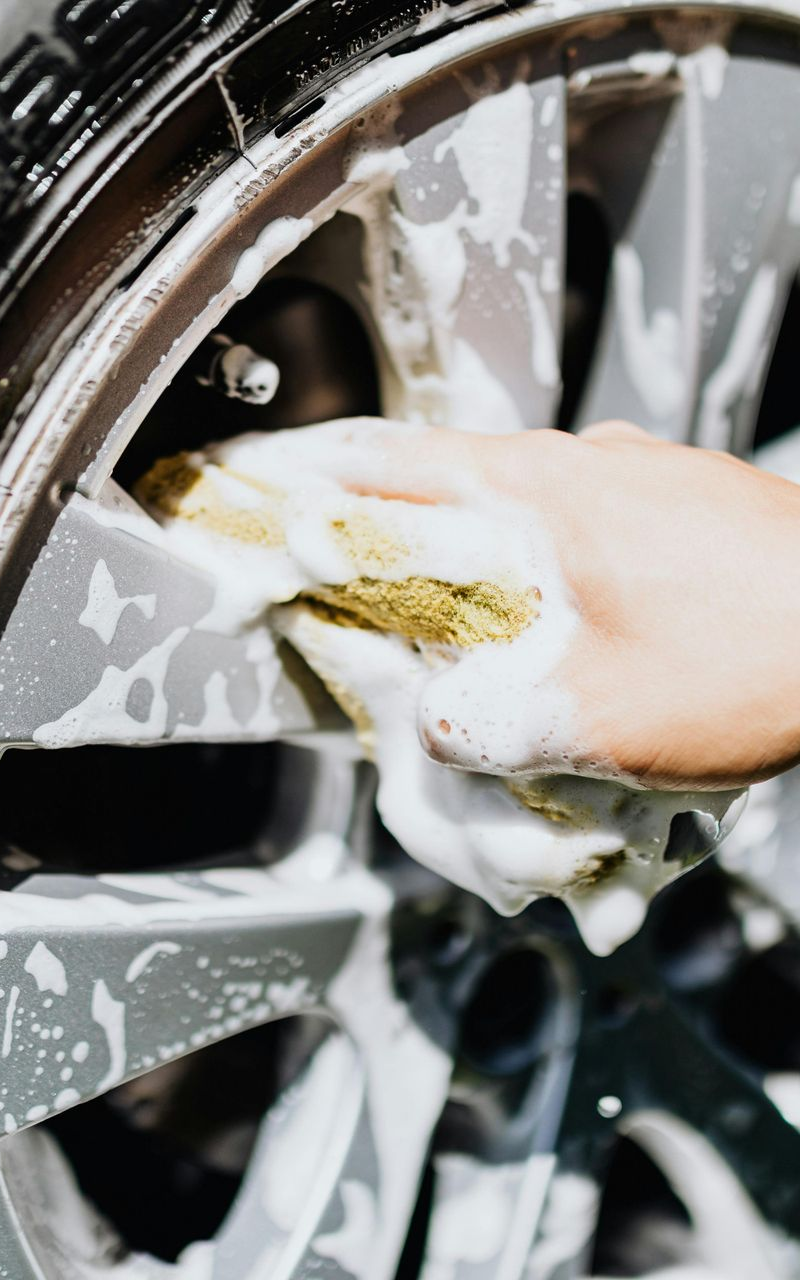 Hand washing a silver car wheel with a soapy sponge.