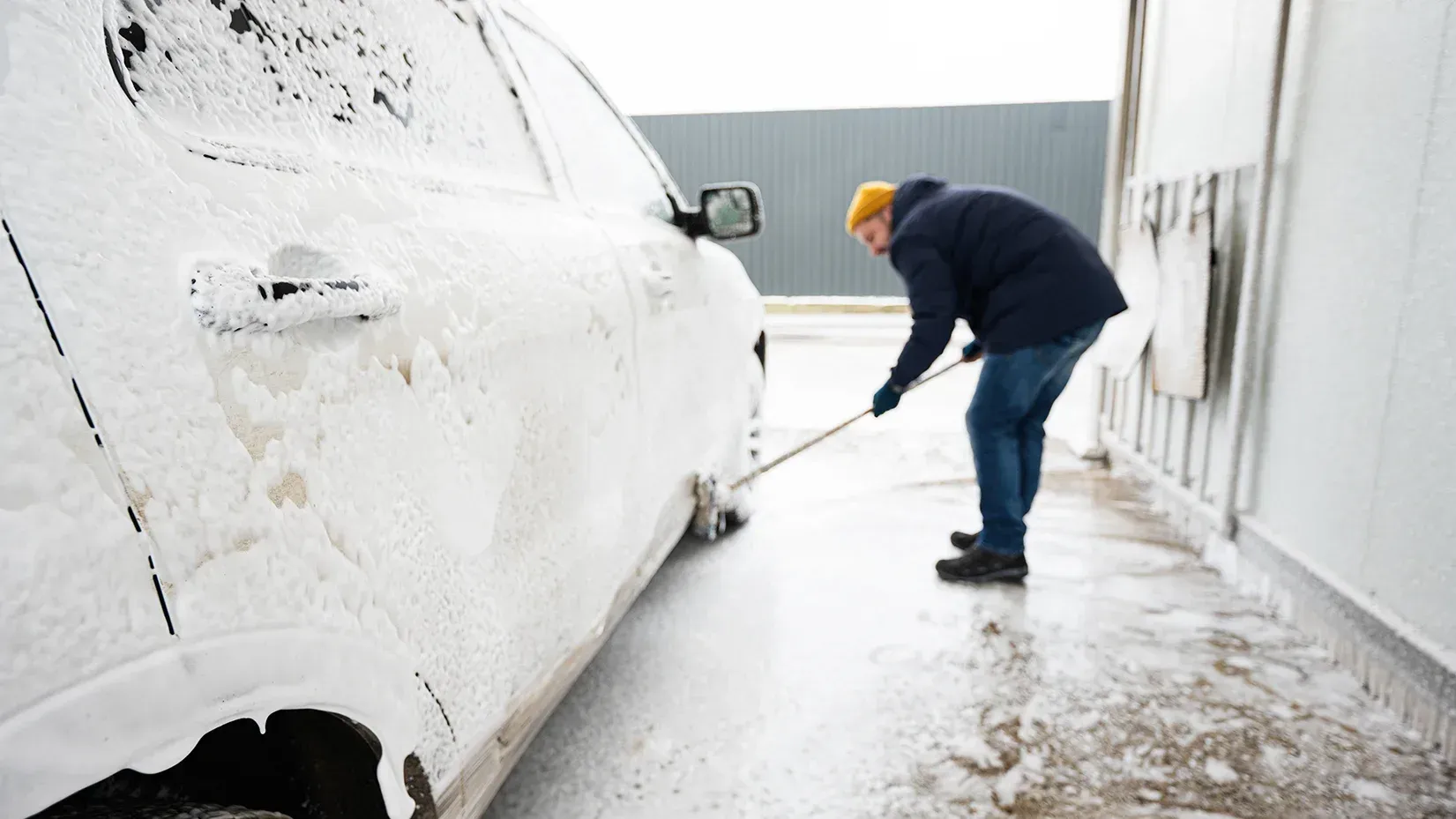 Person washing a white car with soap and brush at a car wash.