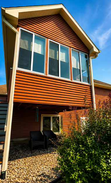 Modern two-story house with red siding, large windows, and a small patio in front of bushes