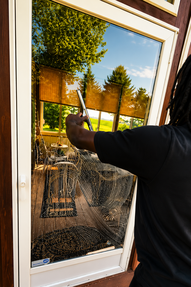 Person painting a white door with a roller, seen through the glass pane.