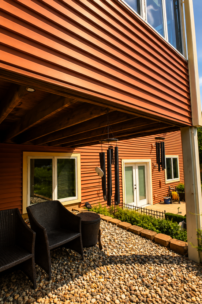 Covered patio with wicker chairs and gravel courtyard beside a modern brick house.