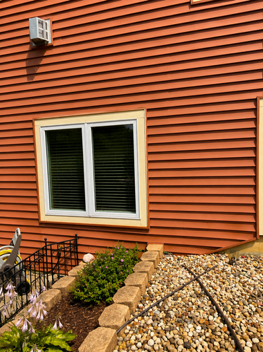 Orange house wall with white-framed window, gravel landscaping, and small shrubs