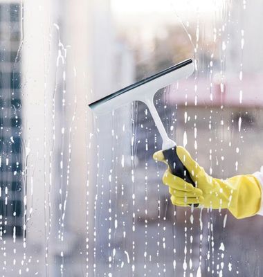 Yellow-gloved hand using a squeegee to clean a rain-streaked window