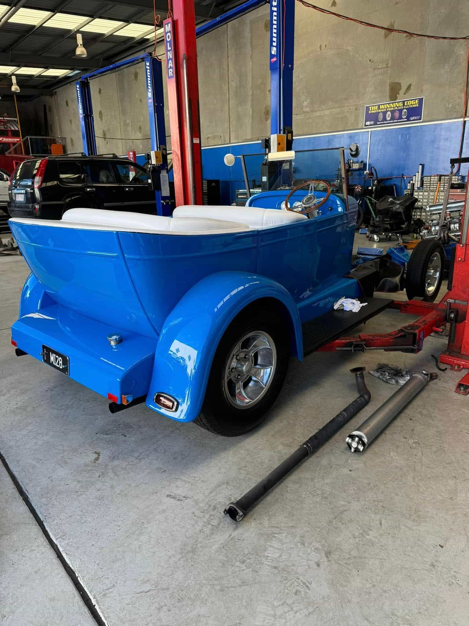 Blue hot rod in a garage, partially assembled. Chrome wheels, exhaust pipes on the floor — Pialba Brake Clutch & Steering Centre in Pialba, QLD