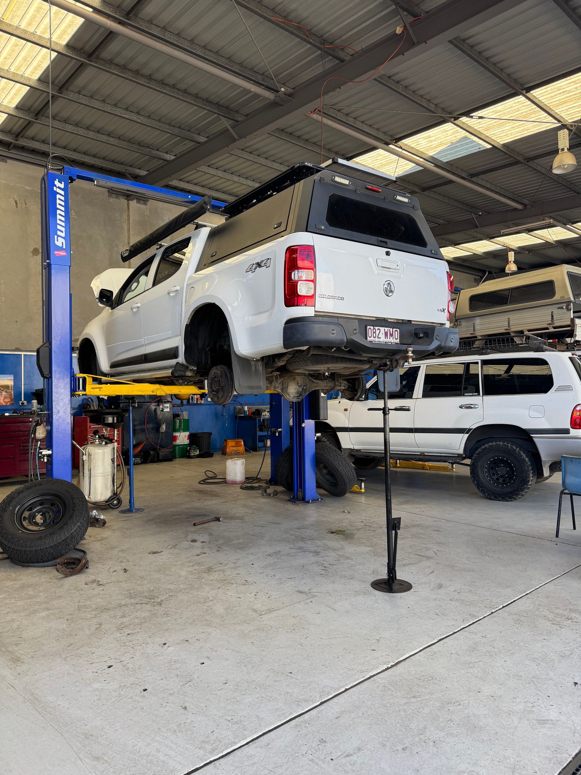 White truck on a lift in a garage, being worked on, with another white truck and equipment in the background — Pialba Brake Clutch & Steering Centre in Pialba, QLD