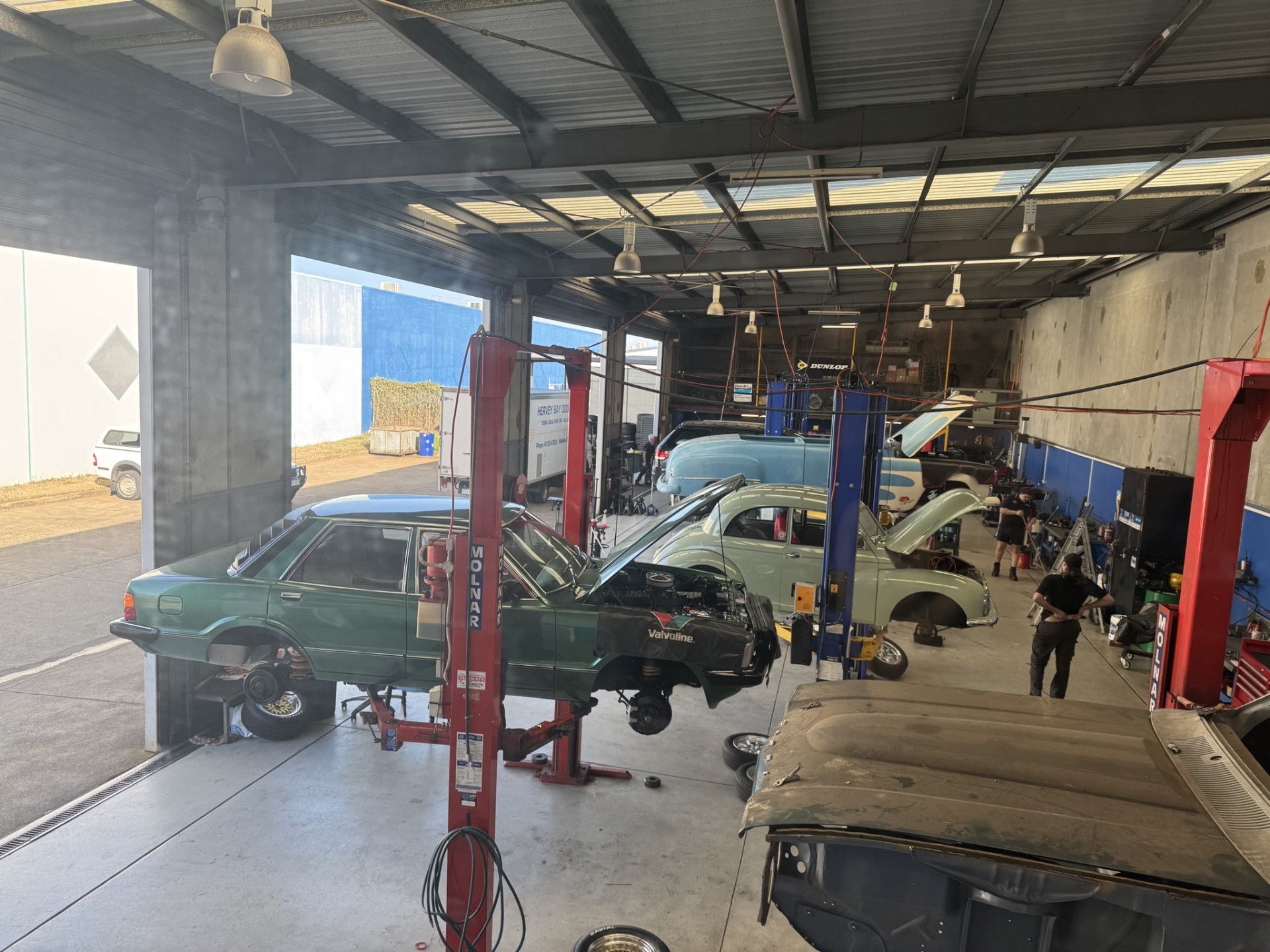 A car repair shop with several cars on lifts, mechanics working, and tools visible — Pialba Brake Clutch & Steering Centre in Pialba, QLD