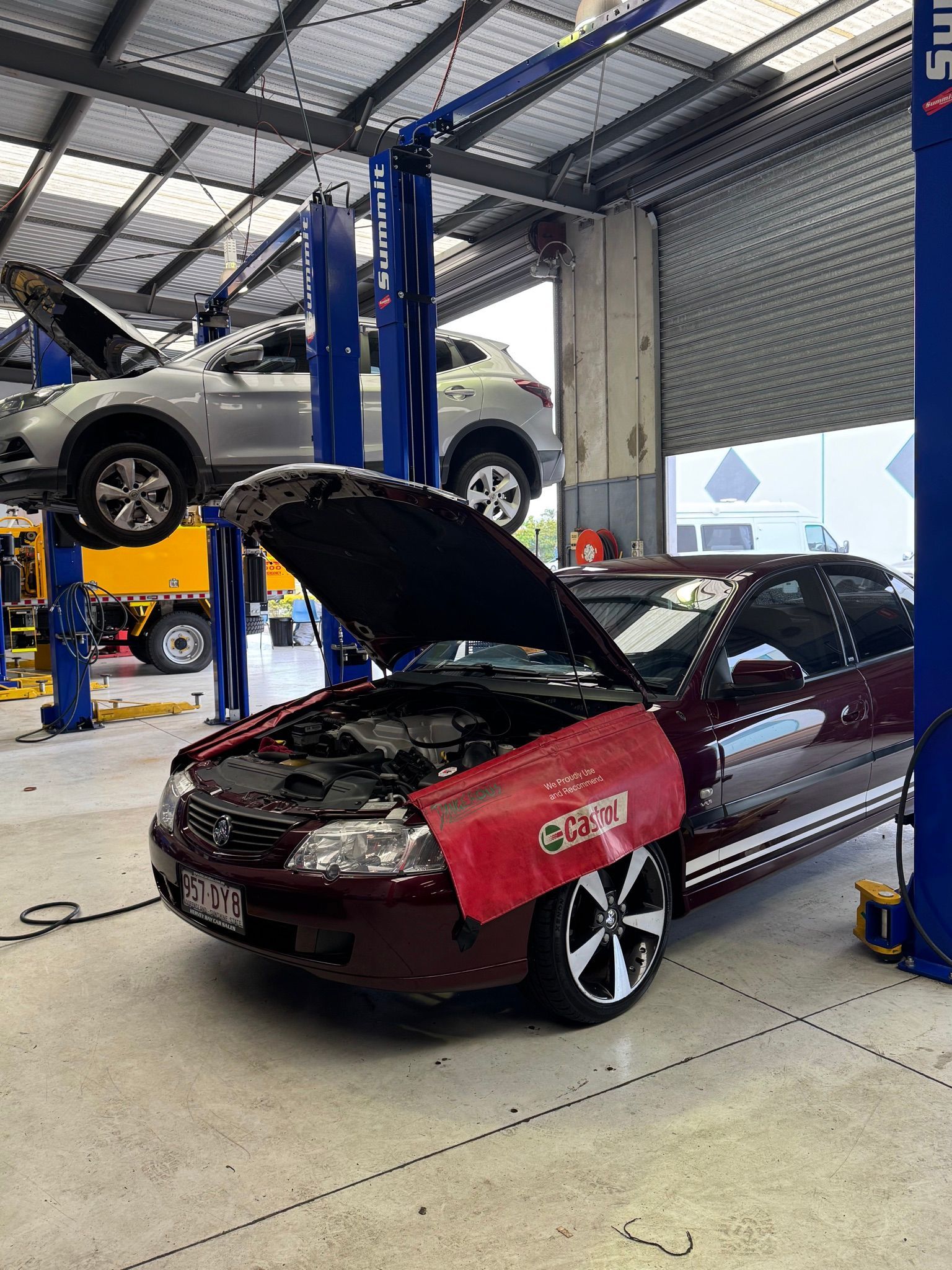 A maroon car with open hood in a garage, a car raised on a lift in the background — Pialba Brake Clutch & Steering Centre in Pialba, QLD