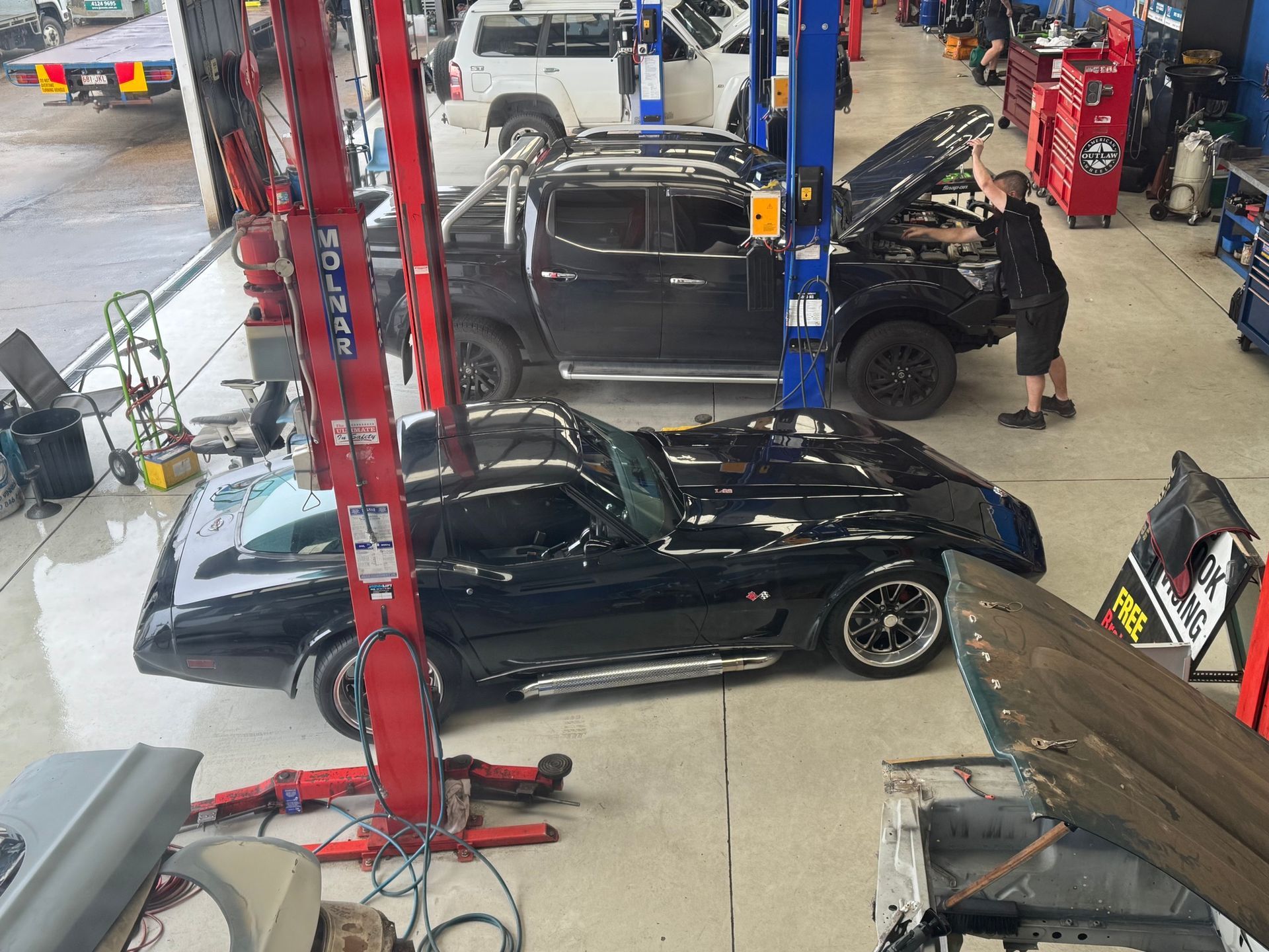 A black Corvette in a mechanic shop, a person working on a truck with its hood open — Pialba Brake Clutch & Steering Centre in Pialba, QLD
