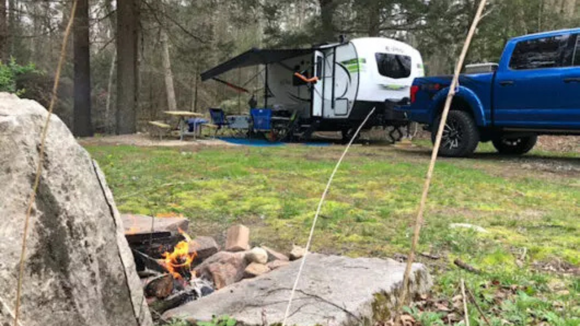A blue truck is parked in front of a camper trailer.
