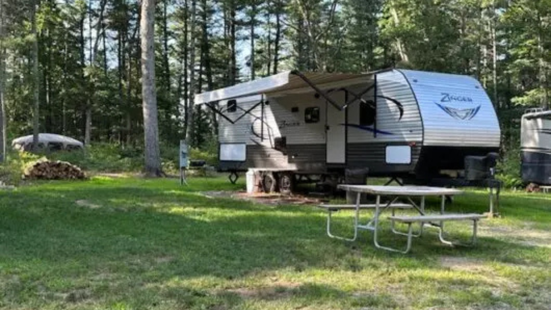 A rv is parked in a grassy area with a picnic table.
