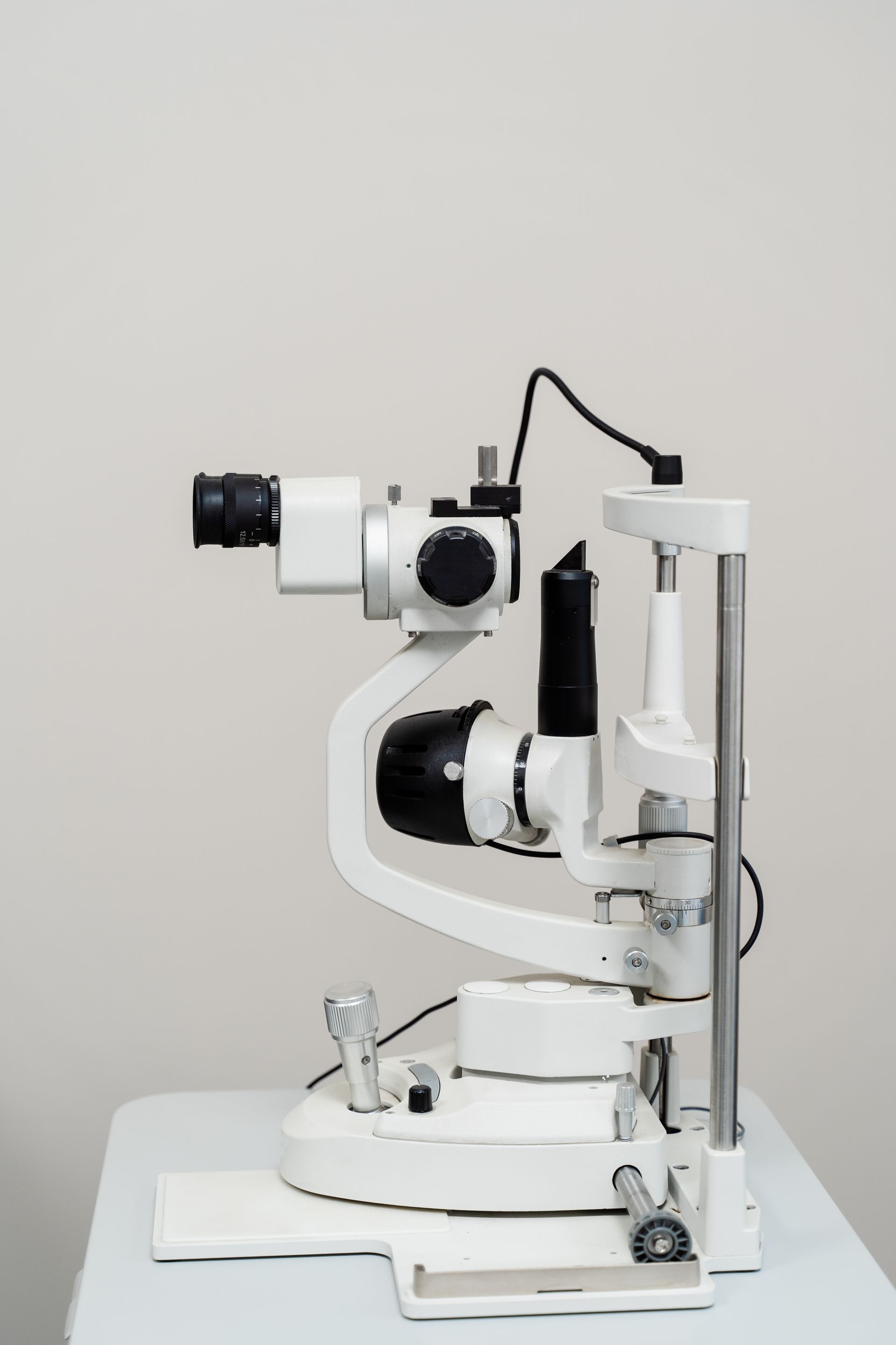 A white slit lamp biomicroscope used for eye examinations, positioned on a table against a neutral background.