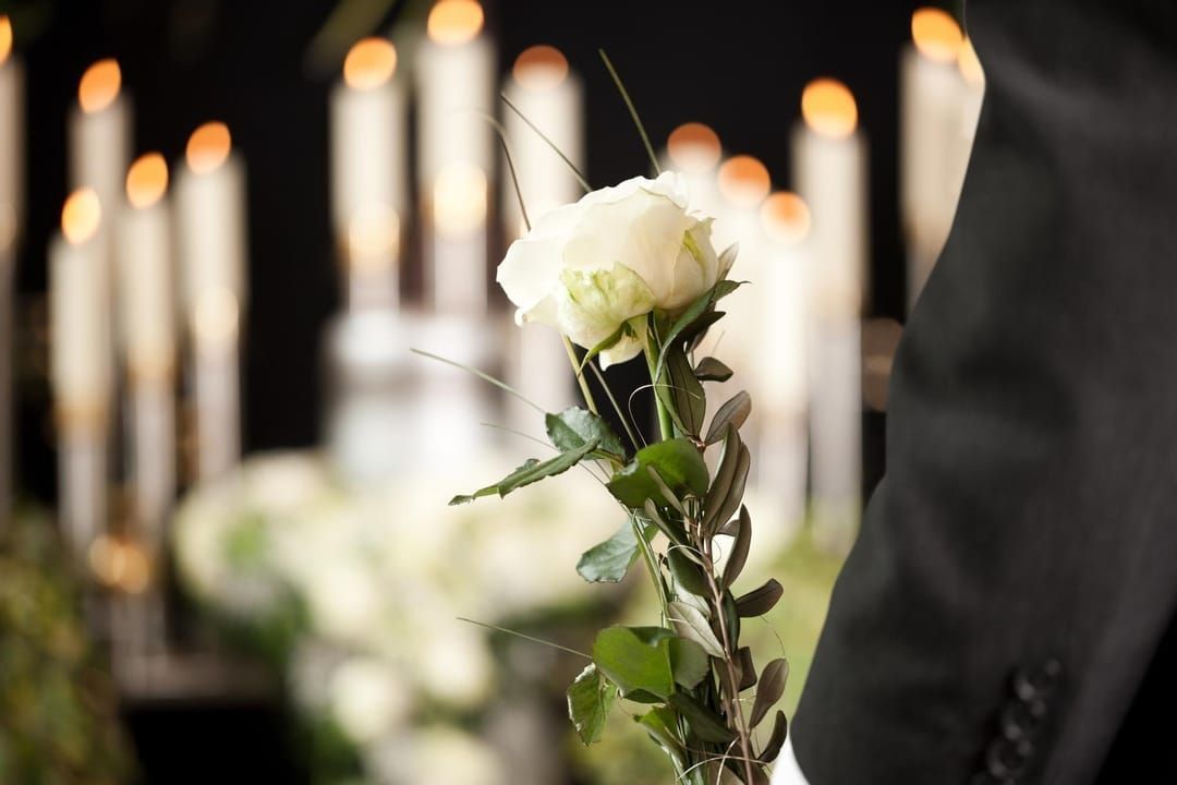 White rose held, with candles and other flowers in blurred background.