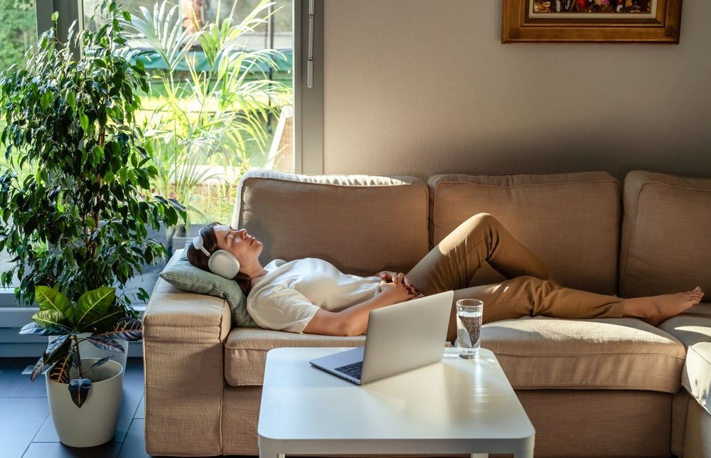 A man is laying on a couch wearing headphones and listening to music.