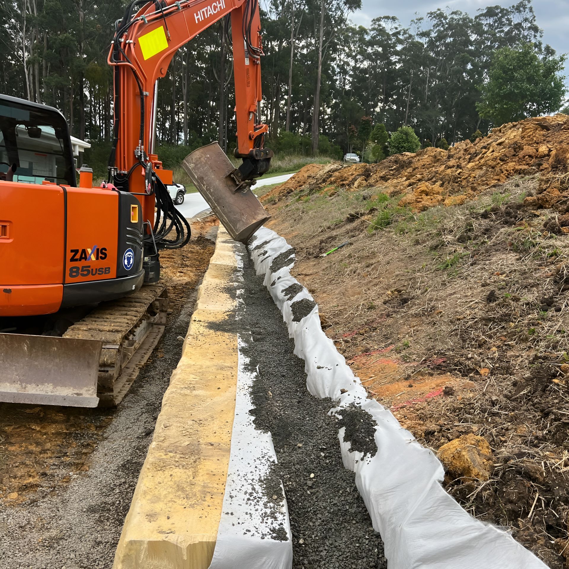 An Excavator is Filling a Trench With Gravel for a Retaining Wall — MG Earthworks and Plant Hire in Gumma, NSW