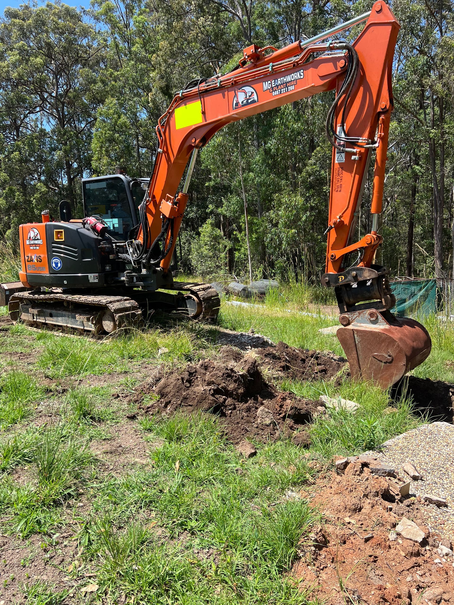 Orange excavator digging in a grassy area with trees in the background.