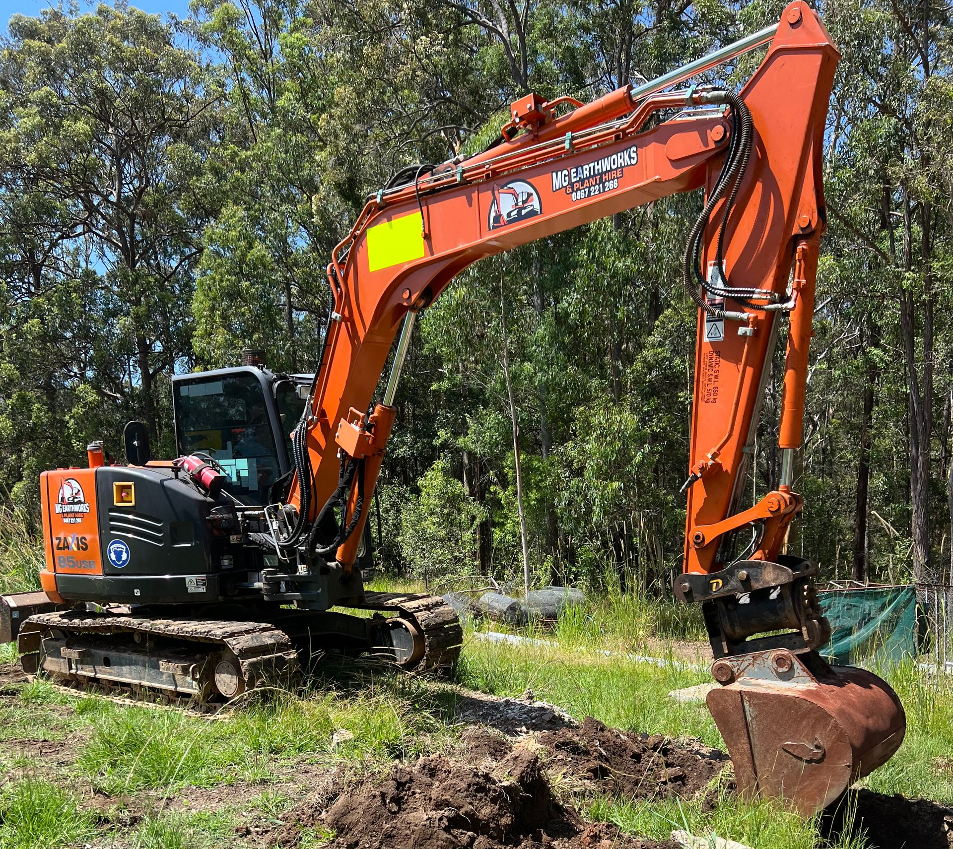 Orange excavator digging in a grassy area with trees in the background.