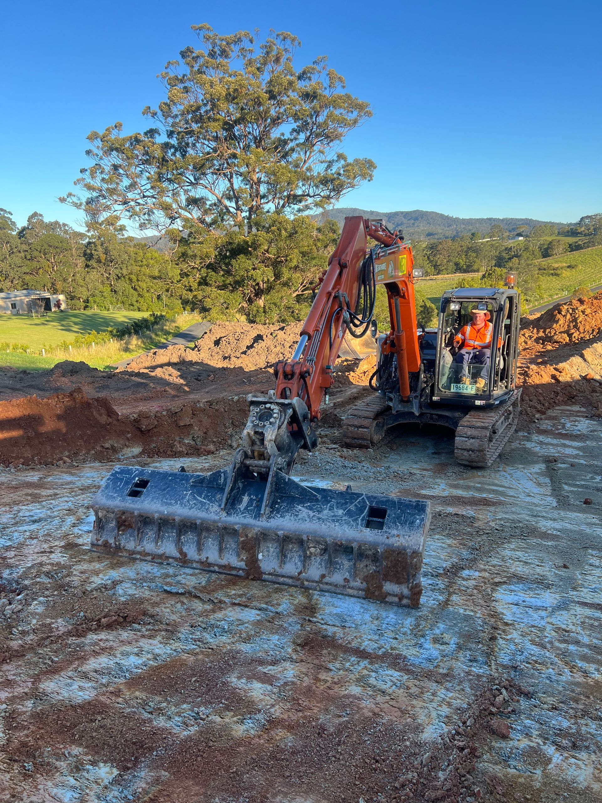 Excavator with wide blade levelling earth at a construction site outdoors on a sunny day.