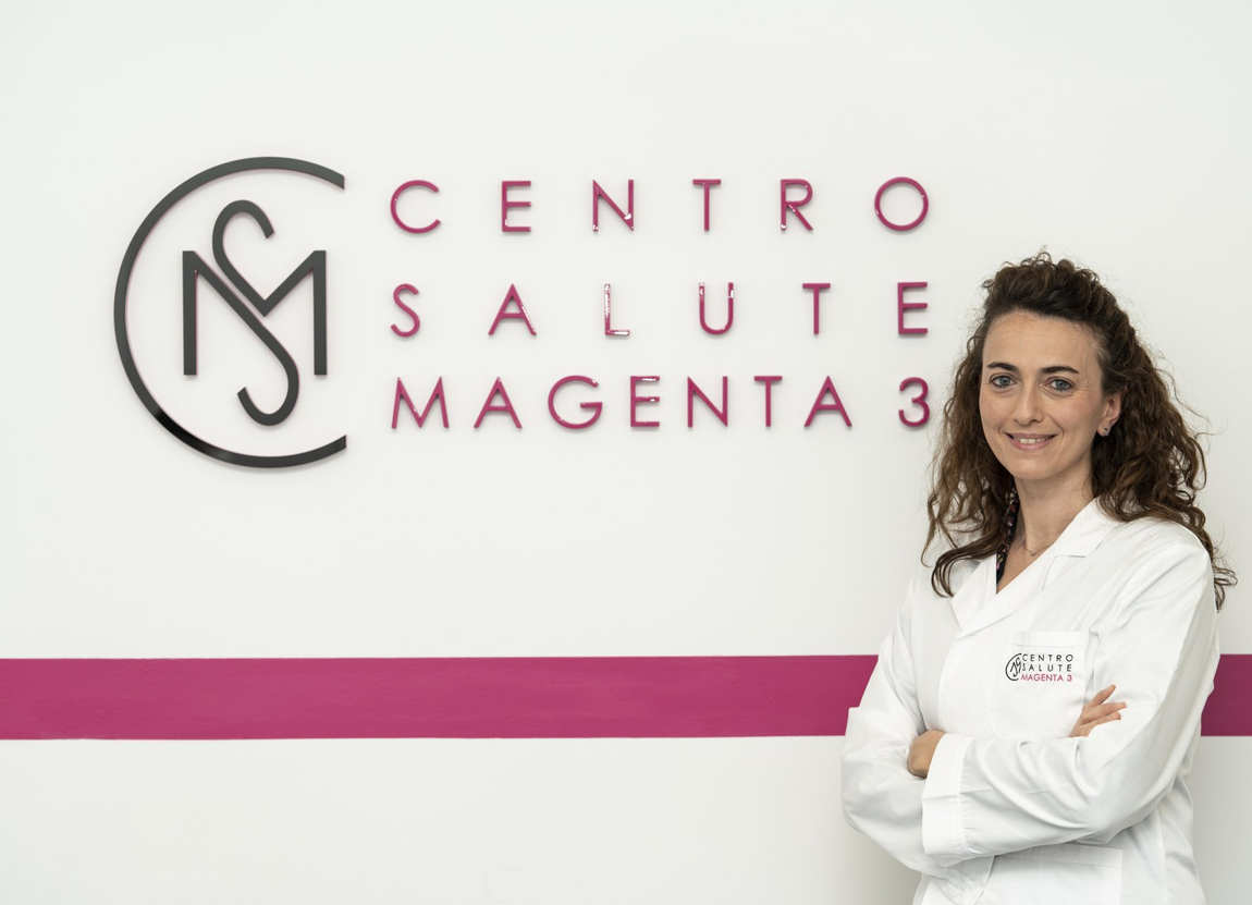 Insegna del Centro Salute Magenta su una parete bianca, con una donna in camice bianco in piedi accanto.