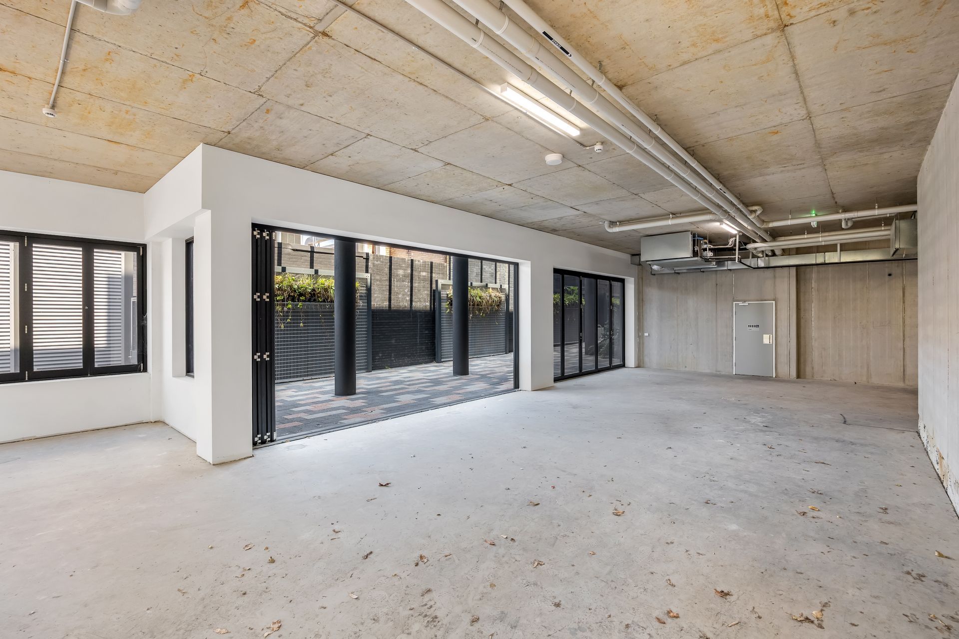 Empty modern room with concrete floor, exposed ceiling, and large glass doors opening to a patio.