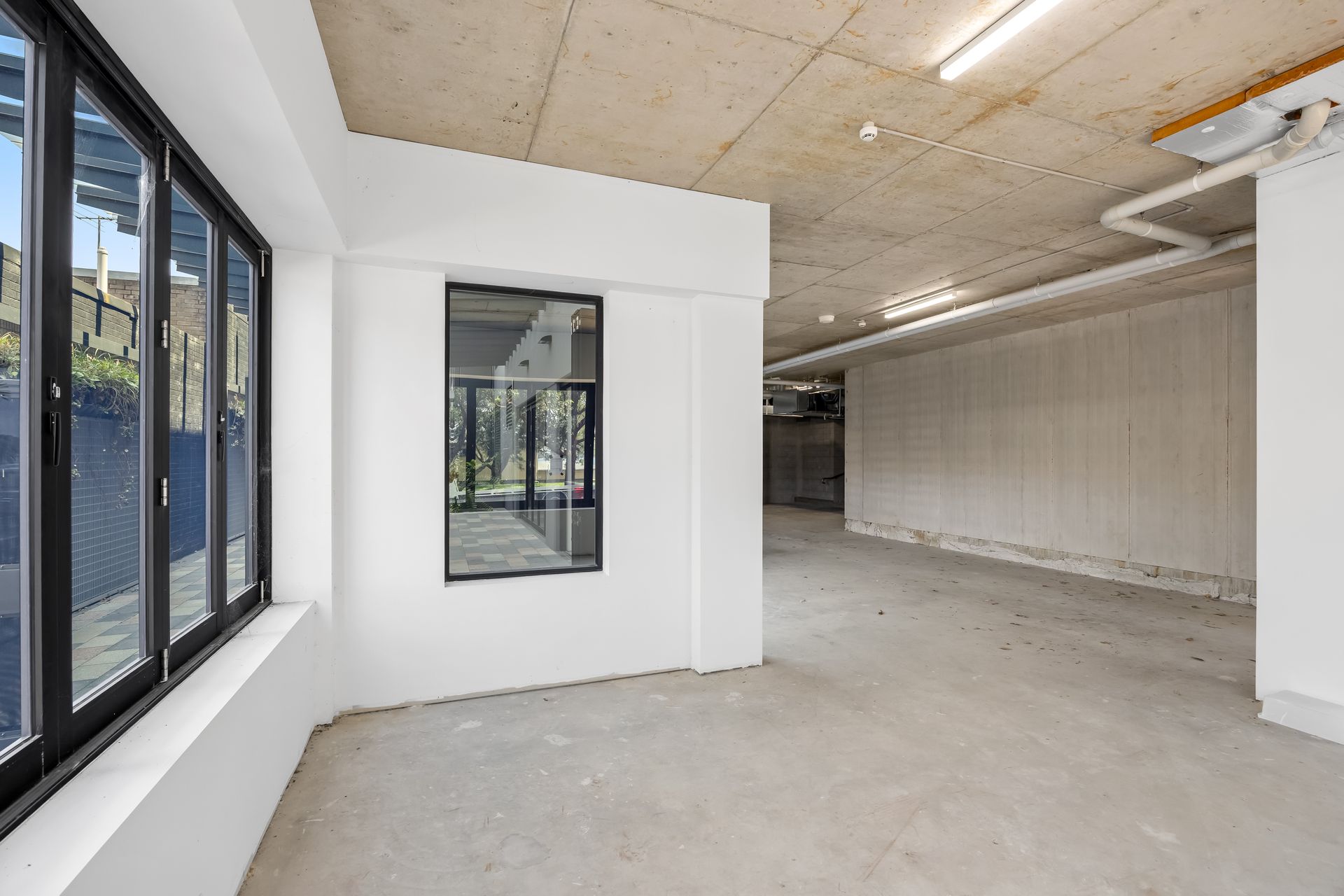 Empty modern industrial room with large windows, white walls, and concrete floors.