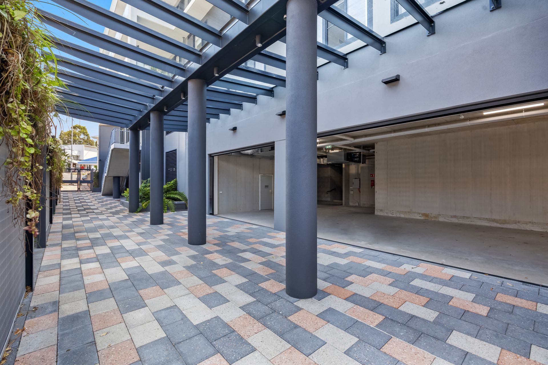 Modern covered walkway with glass canopy, gray columns, and patterned tile pavement