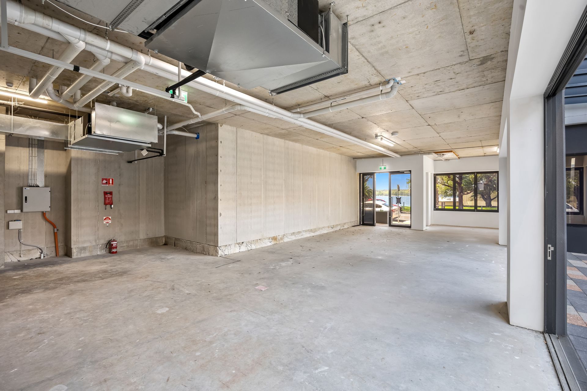 Empty unfinished office space with concrete floors, exposed ceiling ducts, and large windows