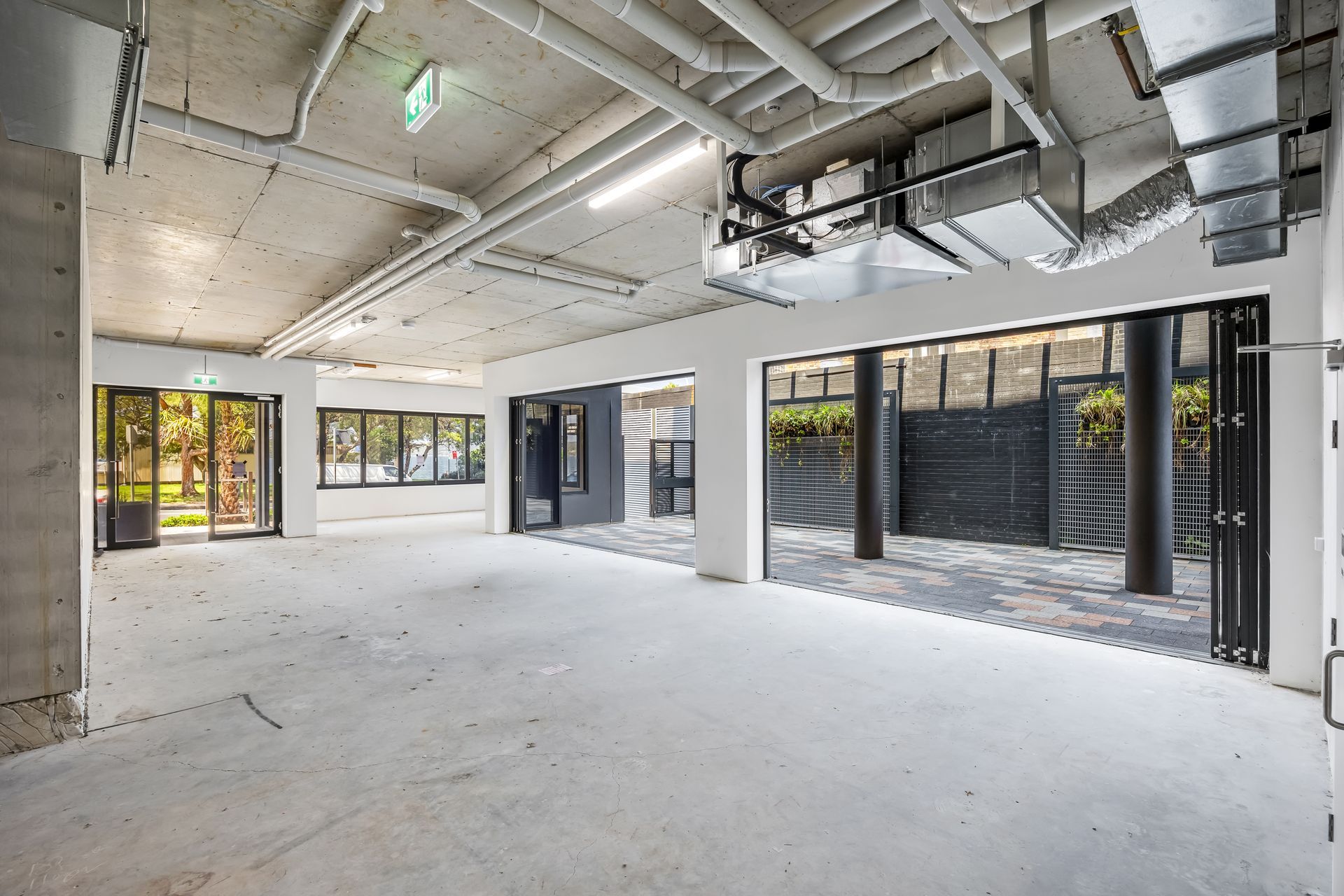 Empty unfinished industrial interior with exposed ductwork, white walls, and large black-framed windows and doors