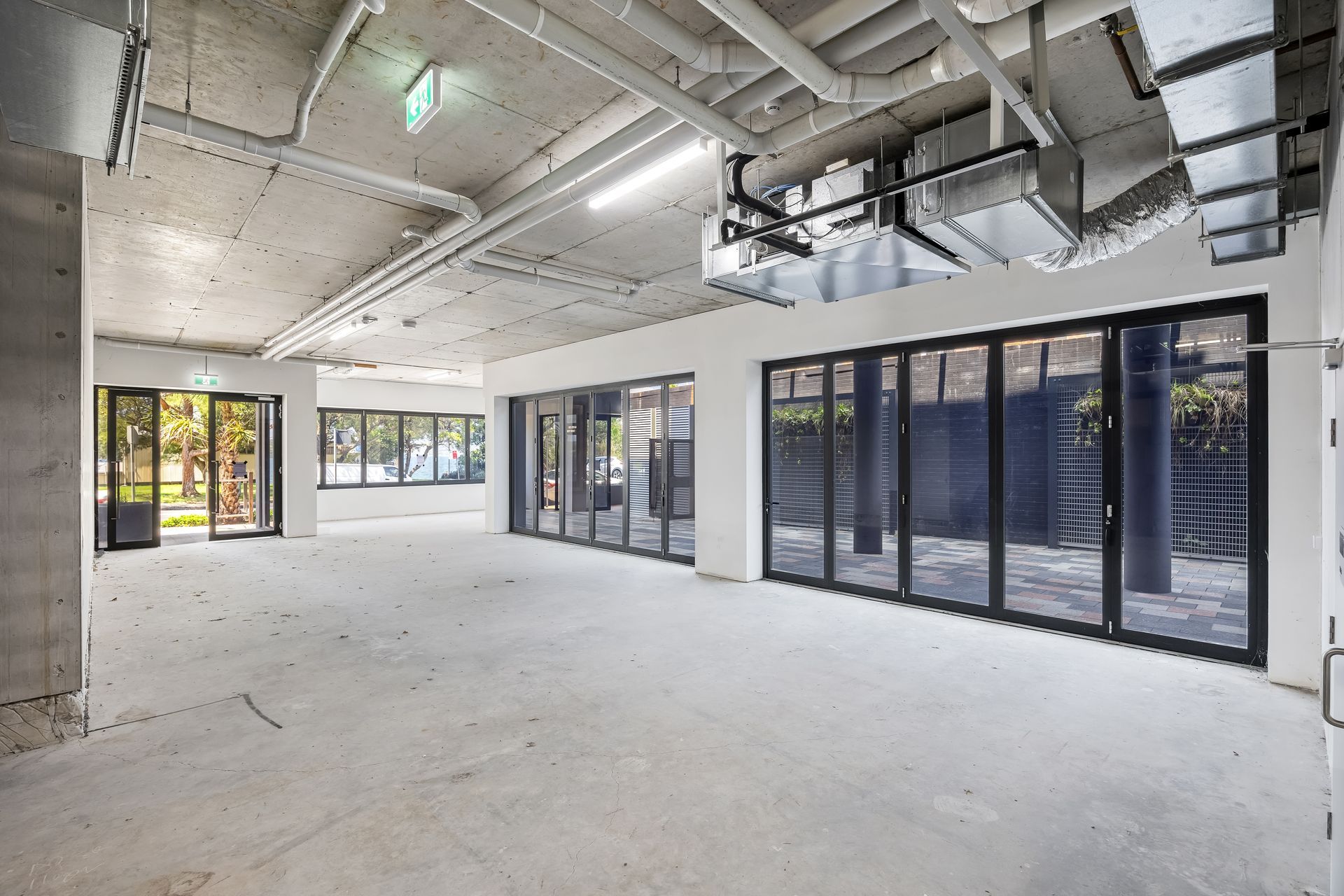 Empty modern office space with exposed ceiling, white walls, and large glass doors and windows