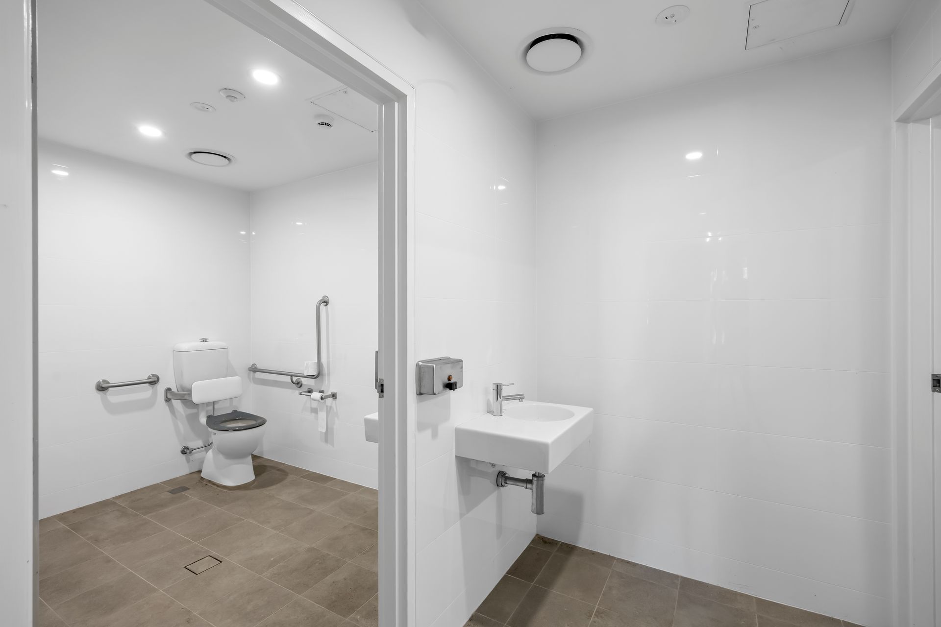 Accessible restroom with toilet, sink, grab bars, and tiled floor in a white interior