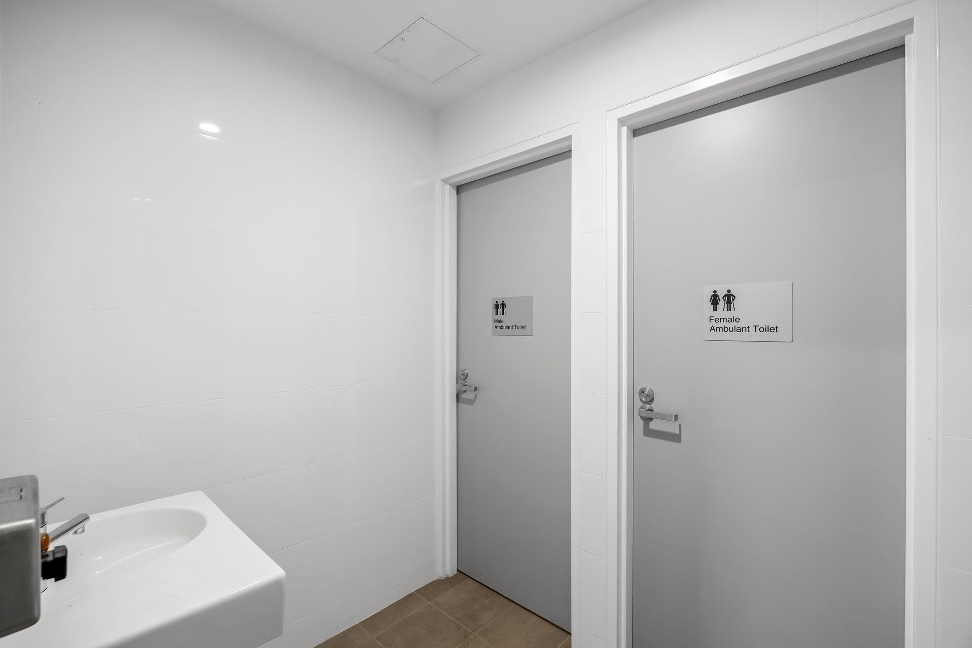 Bright white restroom with two gray stall doors and a sink in the corner.
