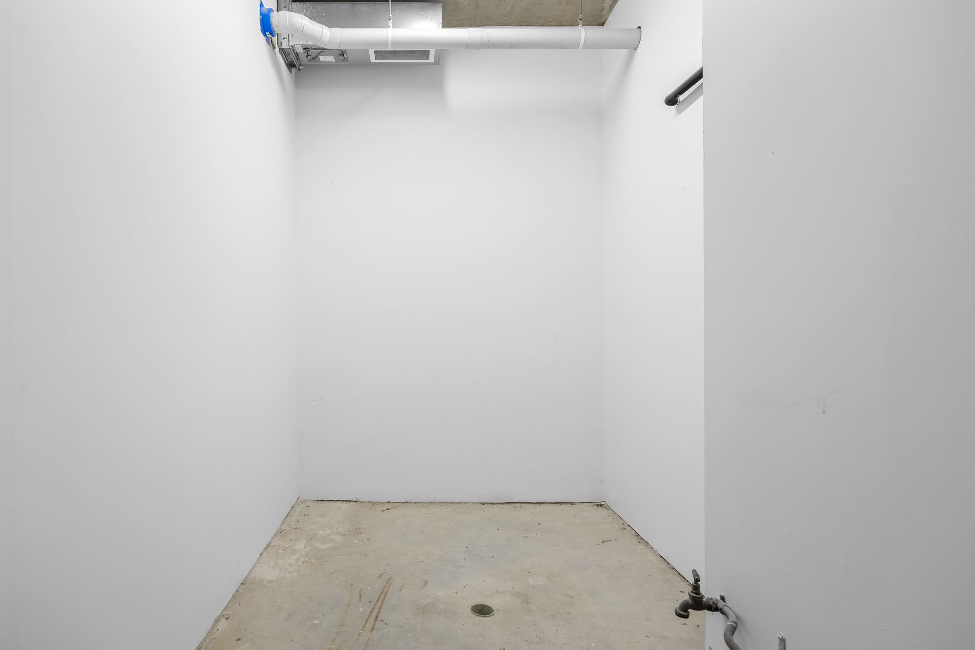 Empty white utility room with concrete floor and exposed ceiling pipes
