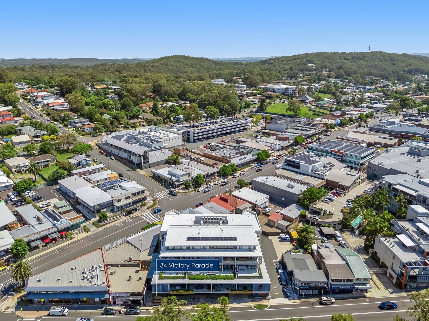 Aerial view of a suburban shopping district with stores, streets, and green hills in the background