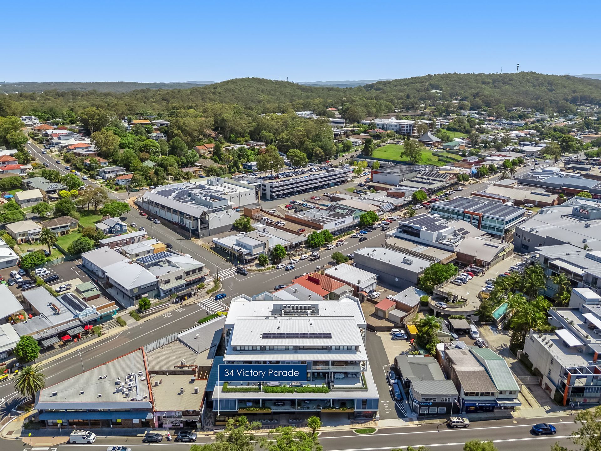 Aerial view of a suburban shopping district with stores, streets, and green hills in the background